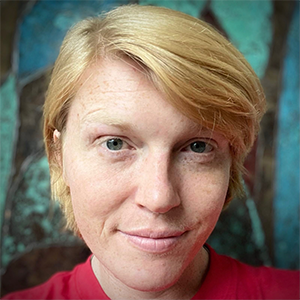 Carrie Cantrell is a white woman with blond hair and blue eyes. She smiles at the camera. A blurred geometric pattern behind her head.